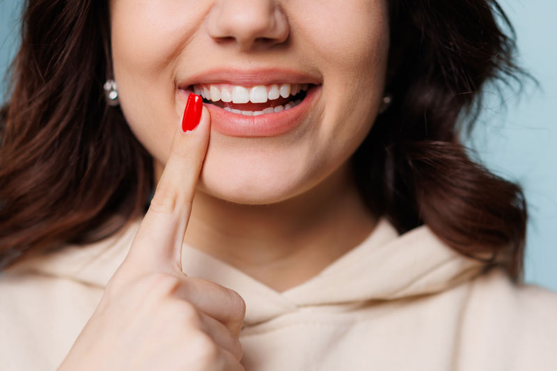 Happy girl showing toothy smile, pointing finger at healthy white teeth. Clinic patient satisfied with dentist service, enamel cleaning, whitening, dental care, correction