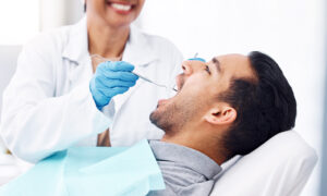 A dentist in a professional setting examines a patient's teeth. the patient is seated in a dental chair, while the dentist uses instruments